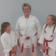 Ruth proudly wearing her Red and White belt award, along with two of her young students